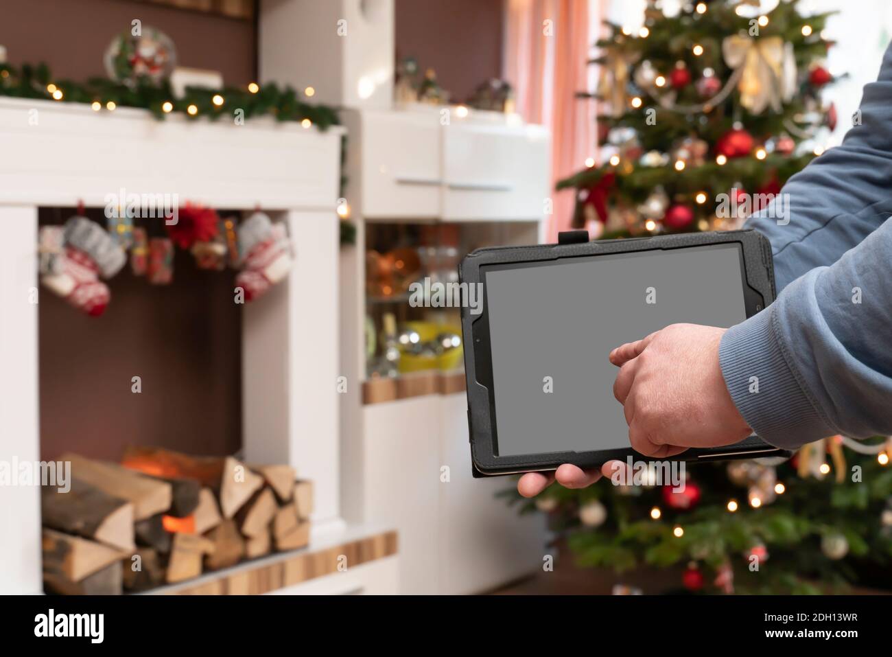 Une main mâle peut contenir une tablette PC. L'homme est debout dans un salon décoré de Christmassy. Console de l'arbre de Noël et de la cheminée. Banque D'Images