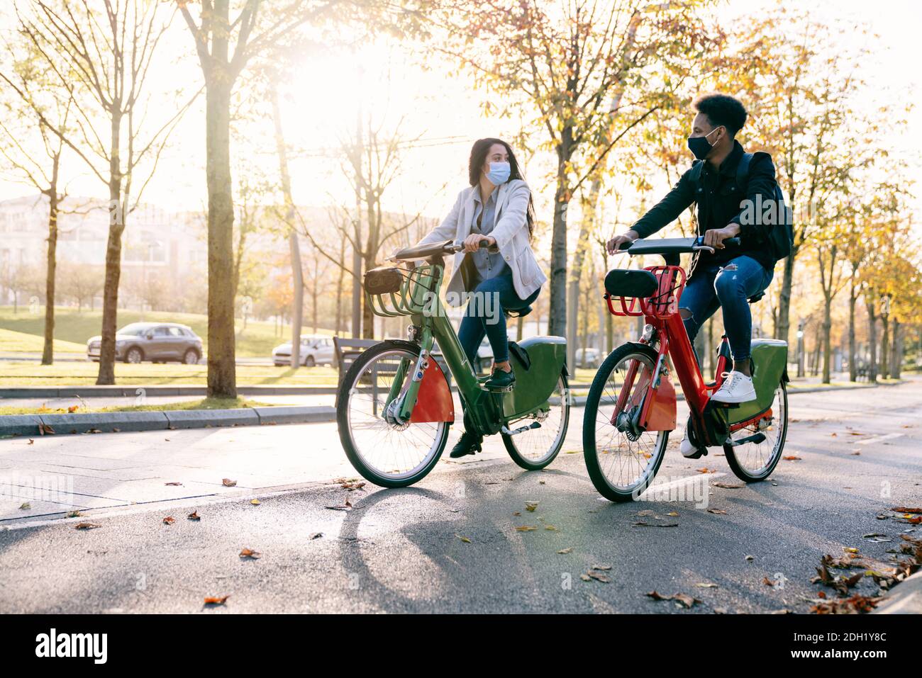 avant de deux jeunes homme et femme, le long d'un piste cyclable avec un vélo électrique de partage dans un beau parc avec de nombreux arbres au coucher du soleil portant un f Banque D'Images