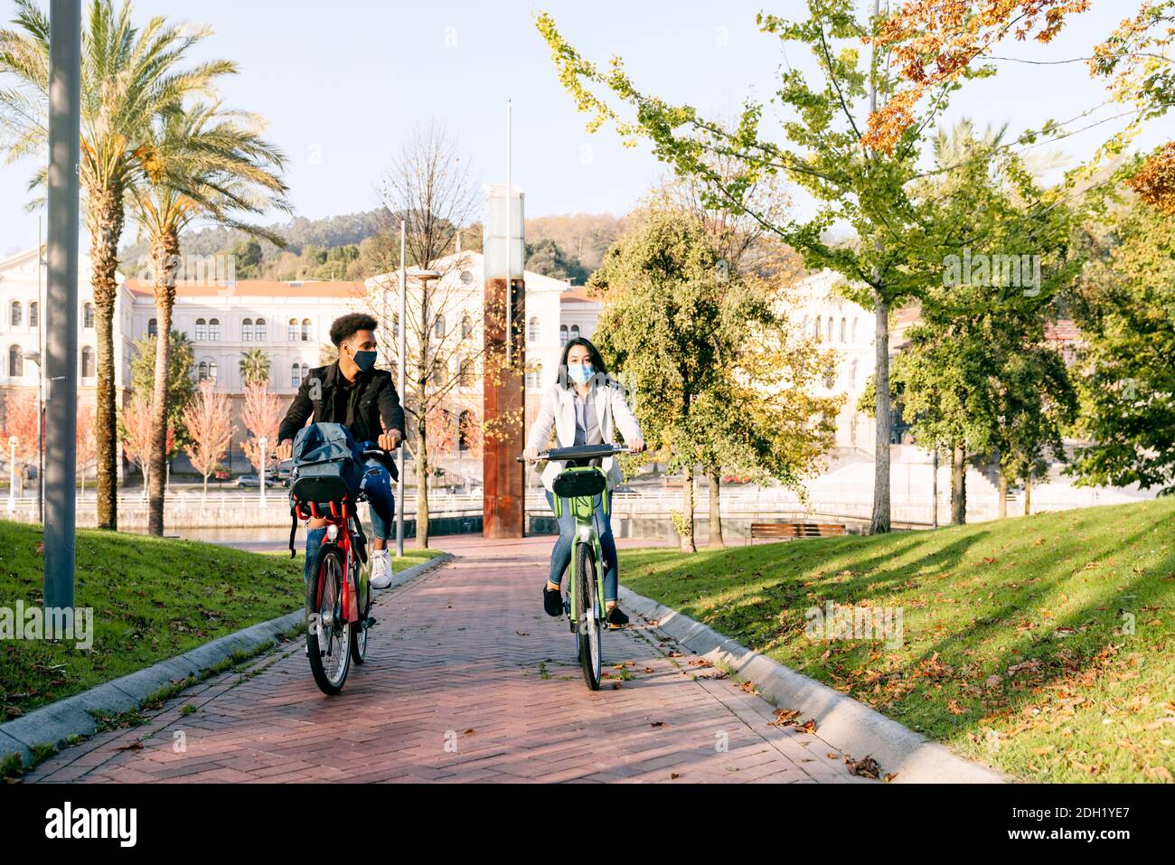 avant de deux jeunes homme et femme, le long d'un piste cyclable avec un vélo électrique de partage dans un beau parc avec de nombreux arbres au coucher du soleil portant un f Banque D'Images