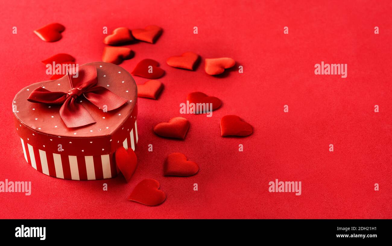 Boîte cadeau en forme de coeur et coeurs sur fond rouge Banque D'Images