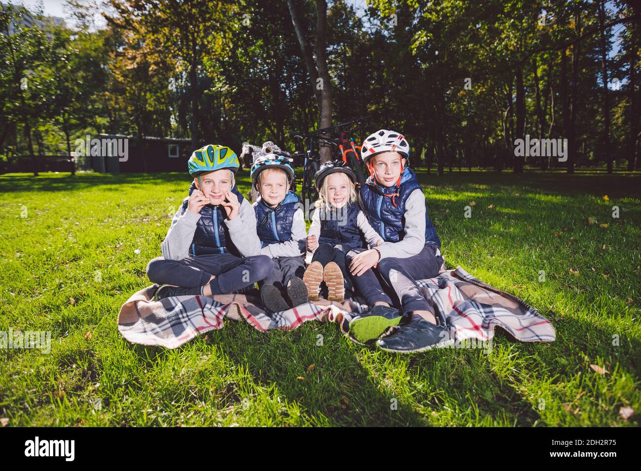 Grande famille d'enfants de race blanche. Trois frères et sœurs assis sur une couverture à l'extérieur du parc. Herbe verte de pelouse de backgro Banque D'Images