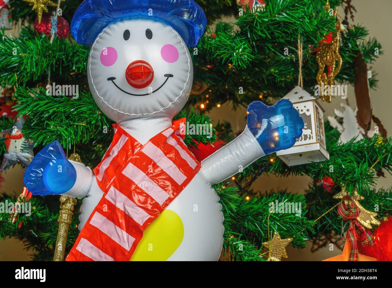 Grand bonhomme de neige gonflable en tant que décoration sur un arbre de Noël. Air soufflé chiffre saisonnier avant illuminé branches artificielles de pin avec des lumières. Banque D'Images