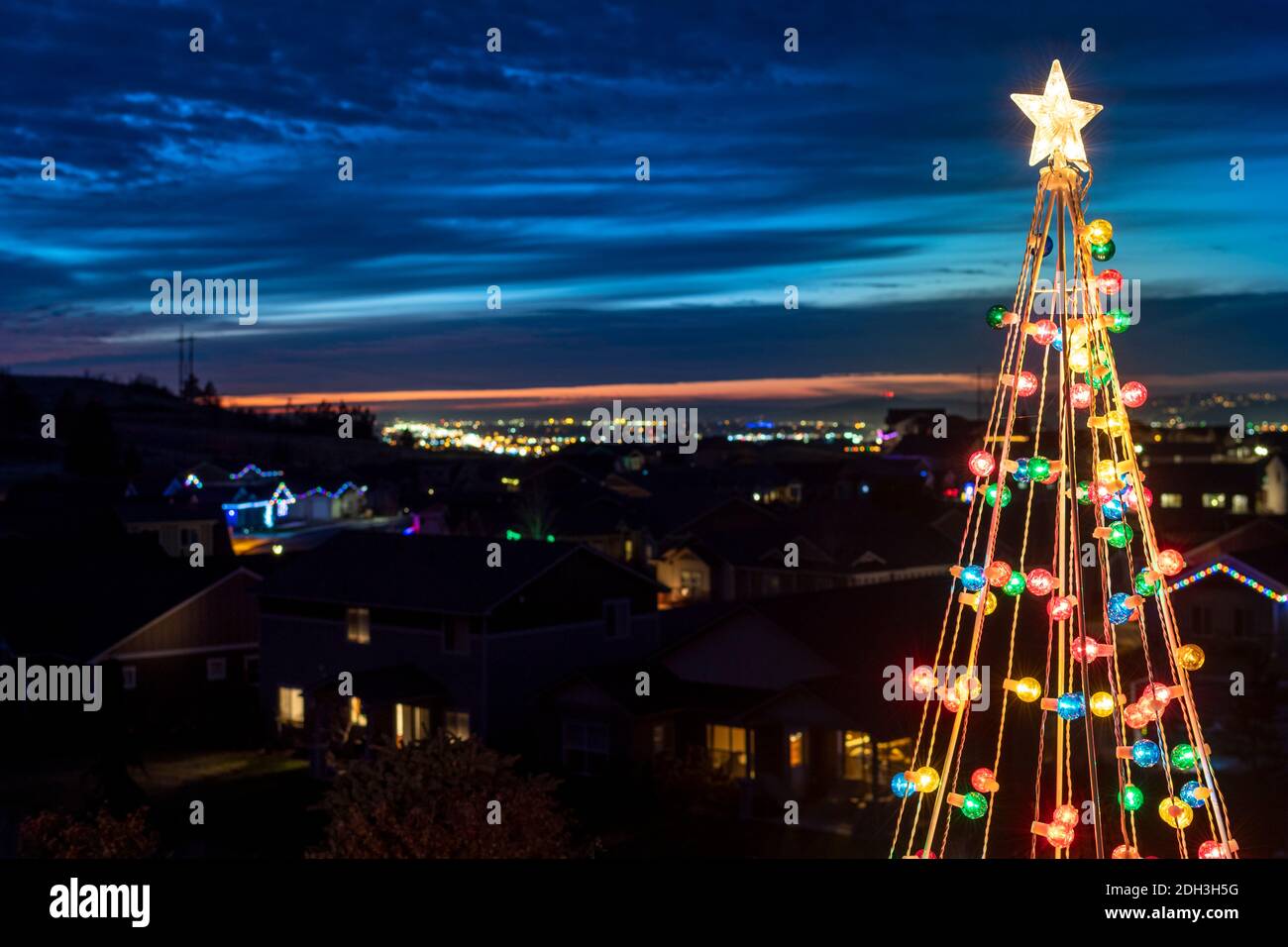 Une décoration colorée de pelouse d'arbre de Noël avec une étoile sur le dessus avec la ligne d'horizon nocturne d'une ville et d'une vallée derrière, à Spokane Washington Etats-Unis Banque D'Images