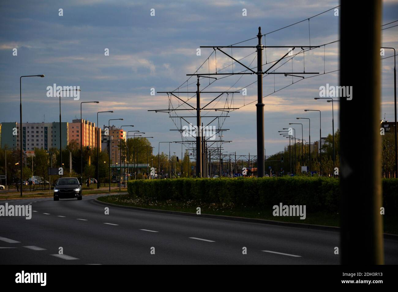 Voiture noire sur la route au printemps à Varsovie Pologne, la nature est verte et lumineuse, le ciel est clair, dans la distance vous pouvez voir un tram et des bâtiments Banque D'Images