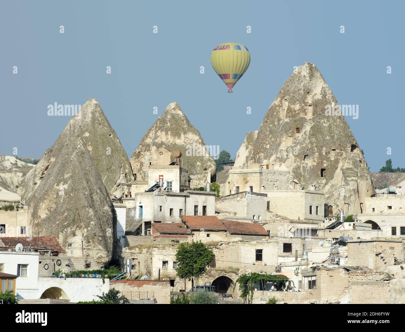 Un ballon d'air chaud au-dessus des cheminées de fées et des maisons dans le village de Goreme, Cappadoce, Turquie Banque D'Images