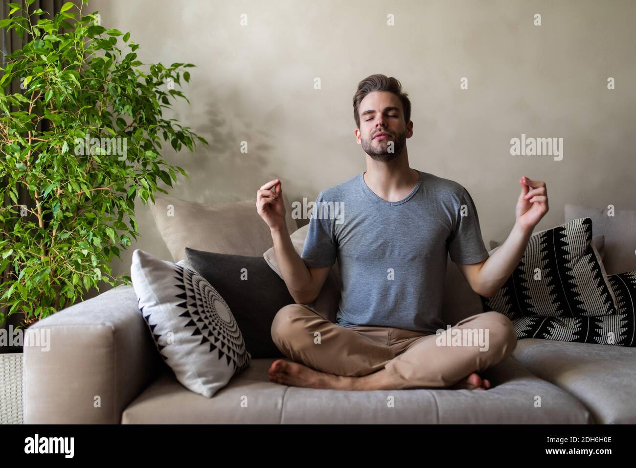 Homme détendu assis avec ses jambes croisées sur le canapé et ses yeux fermés faire une certaine méditation Banque D'Images
