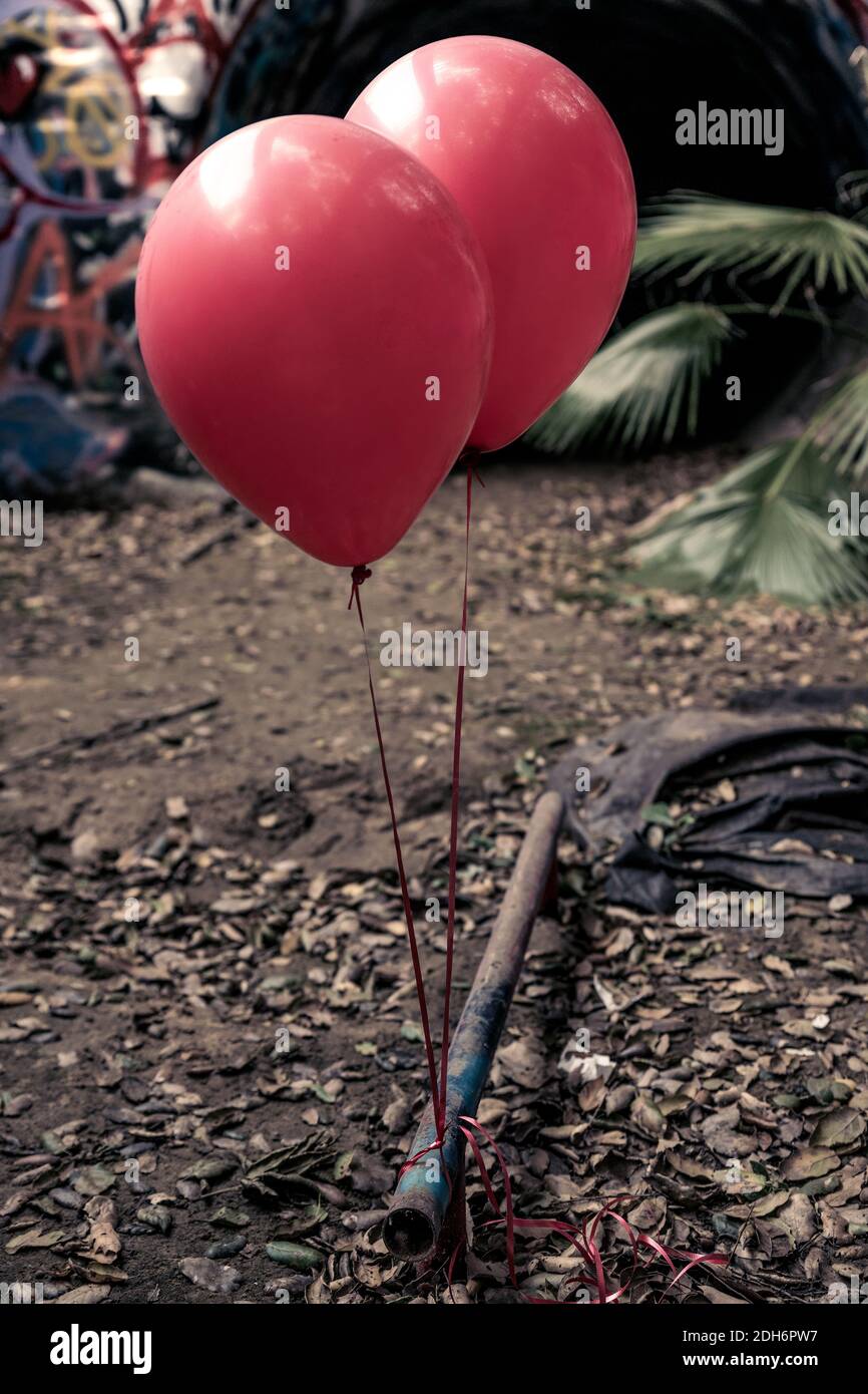 Ballons rouges vibrants attachés à un tuyau rouillé dans un égout de Californie. Graffiti aligne les murs en arrière-plan. Banque D'Images