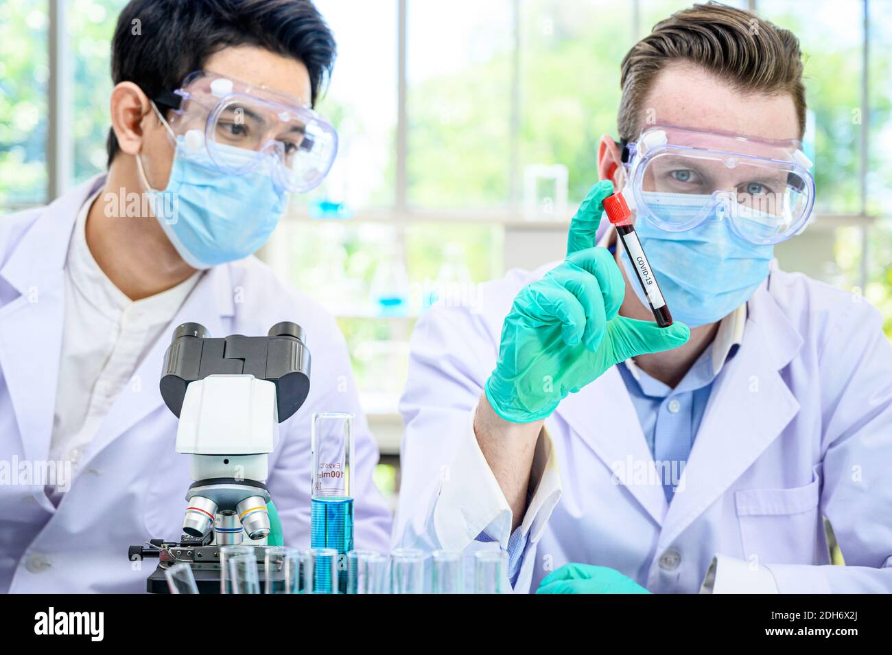 Couple de scientifiques mâles portant une combinaison de protection tenant le vaccin du coronavirus et travaillant avec de nombreux équipements de laboratoire pour la recherche de vaccins en laboratoire. Viru Banque D'Images