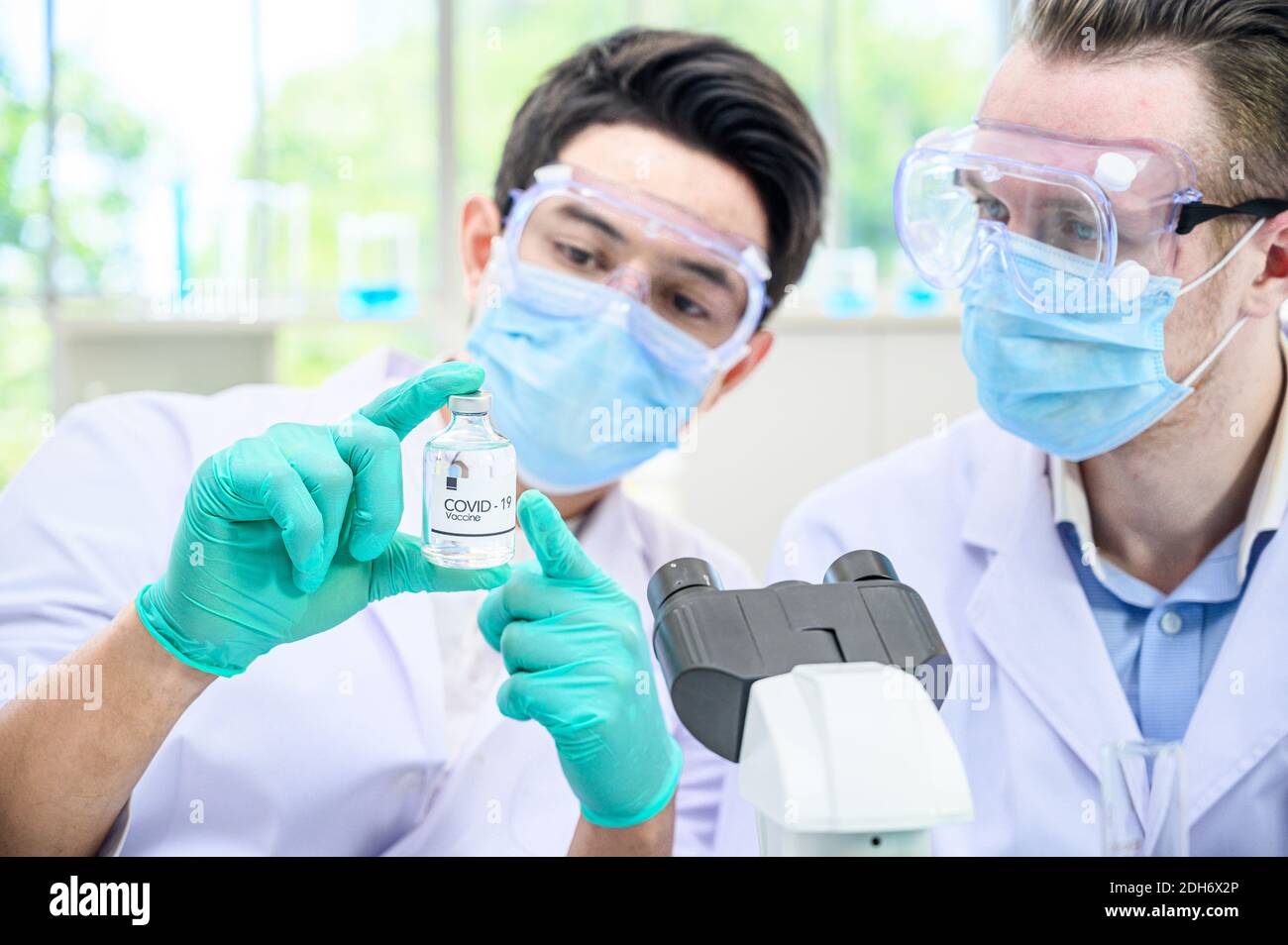 Couple de scientifiques mâles portant une combinaison de protection tenant le vaccin du coronavirus et travaillant avec de nombreux équipements de laboratoire pour la recherche de vaccins en laboratoire. Viru Banque D'Images