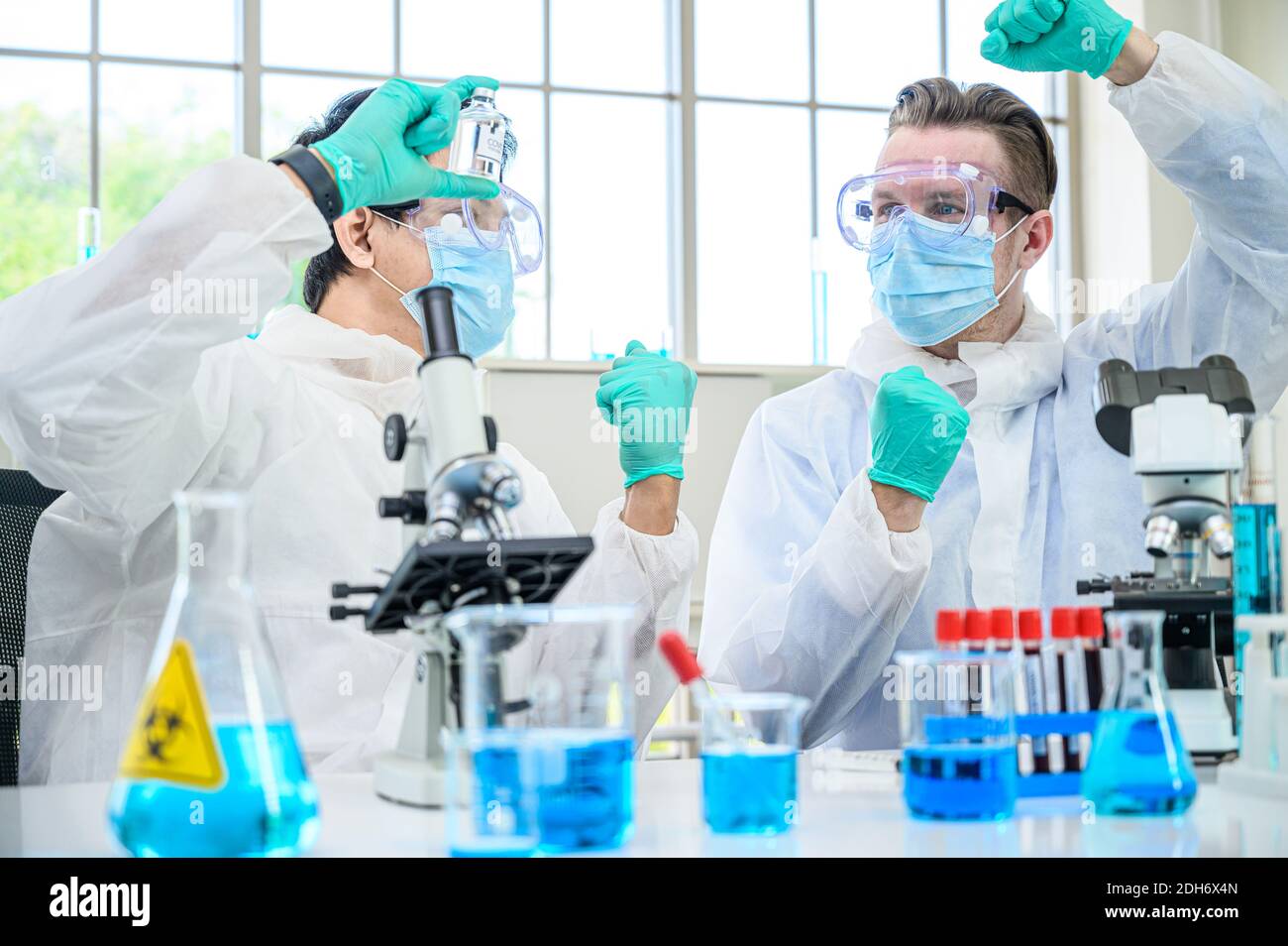 Couple de scientifiques mâles portant une combinaison de protection tenant le vaccin du coronavirus et travaillant avec de nombreux équipements de laboratoire pour la recherche de vaccins en laboratoire. Viru Banque D'Images