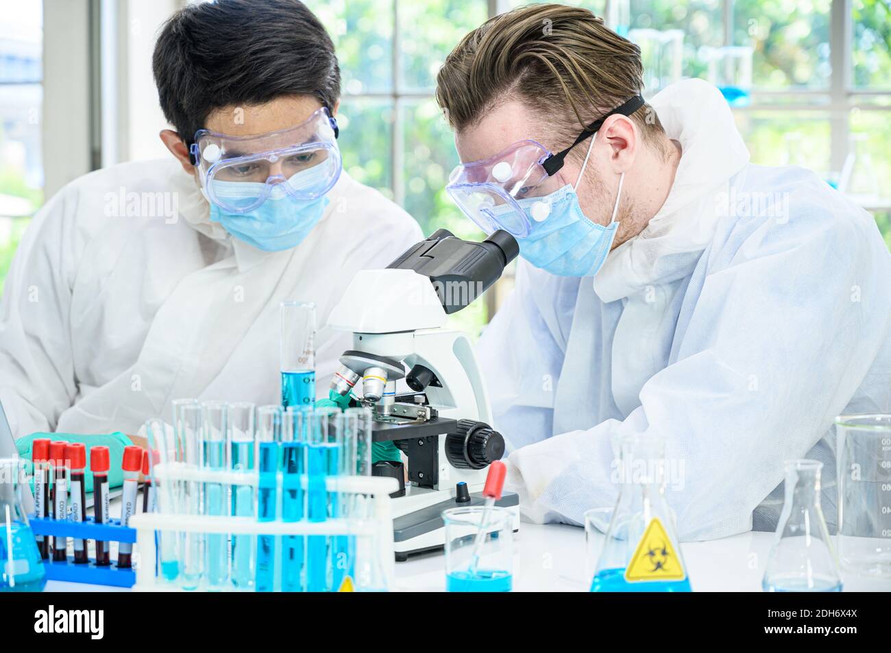Couple de scientifiques mâles portant une combinaison de protection travaillant avec le microscope et de nombreux équipements de laboratoire pour la recherche du vaccin contre le coronavirus en laboratoire. Virus réf Banque D'Images