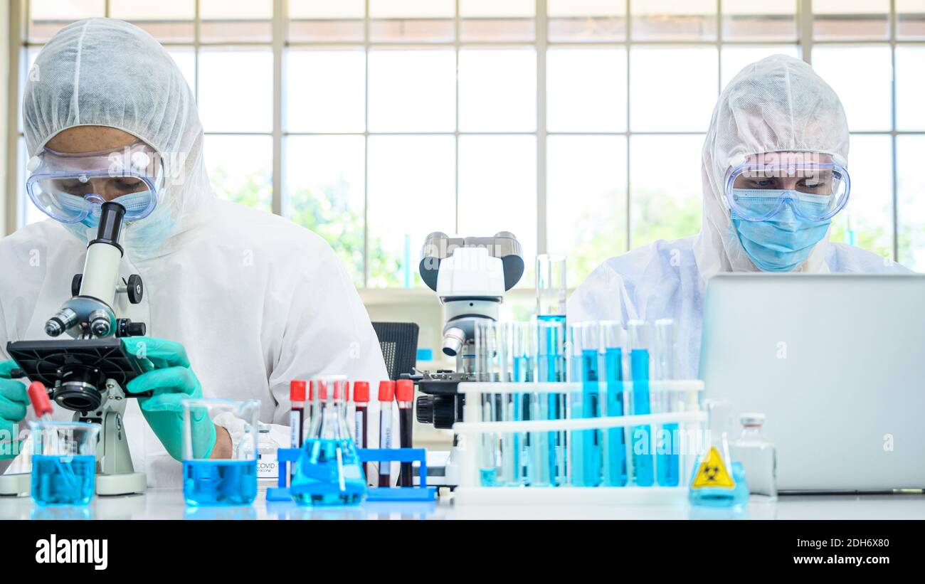 Couple scientifique mâle portant une combinaison de protection travaillant avec de nombreux équipements de laboratoire et ordinateur portable pour la recherche de vaccins en laboratoire. Traitement médical Banque D'Images
