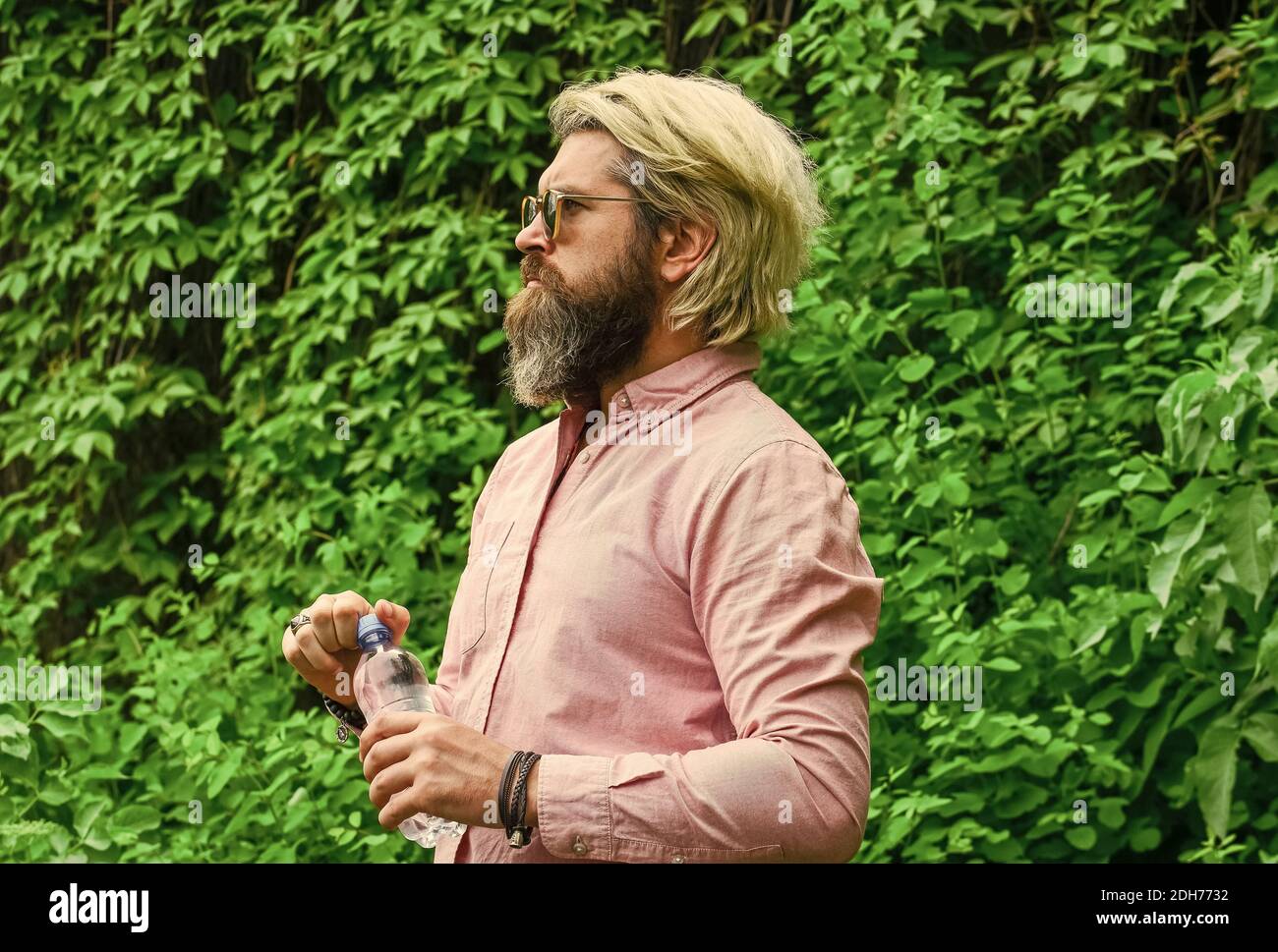 Un gars assoiffé qui boit de l'eau en bouteille Un mode de vie sain. Chaleur estivale. Boire de l'eau claire. Sécurité et santé. Équilibre de l'eau. Homme barbu touriste eau potable bouteille plastique nature fond. Banque D'Images