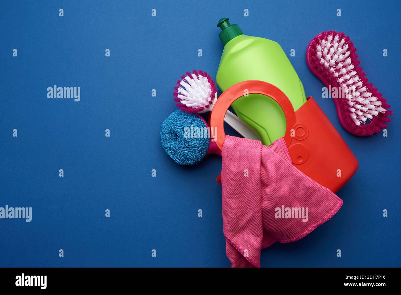 Panier rose avec éponges de lavage, brosses et agent de nettoyage dans une bouteille en plastique vert sur un bac bleu Banque D'Images