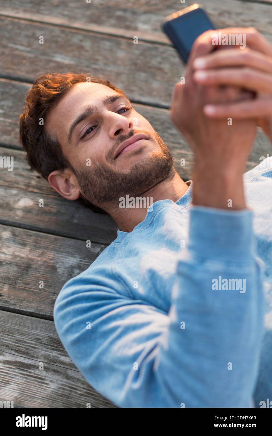 Vue en grand angle de l'homme qui utilise un téléphone portable lorsqu'il est allongé sur la jetée en bois Banque D'Images