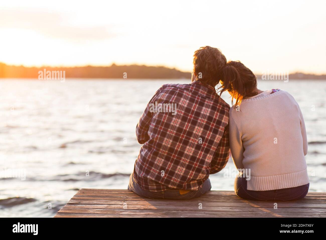 Vue arrière d'un couple aimant assis sur la jetée contre la mer au coucher du soleil Banque D'Images