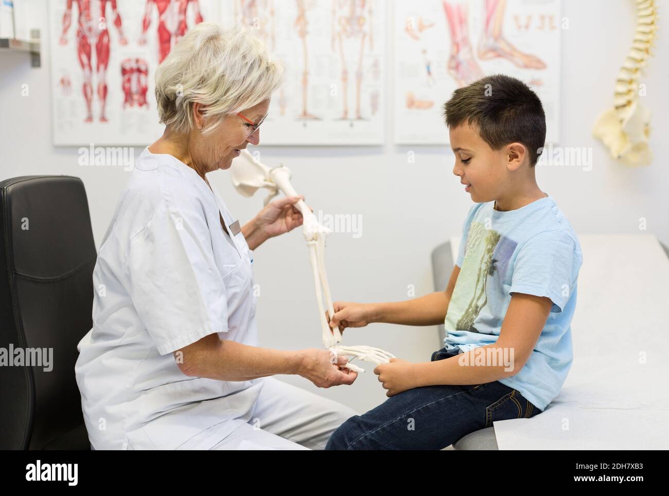 Orthopédiste femelle senior montrant le mannequin de main au garçon à la clinique Banque D'Images