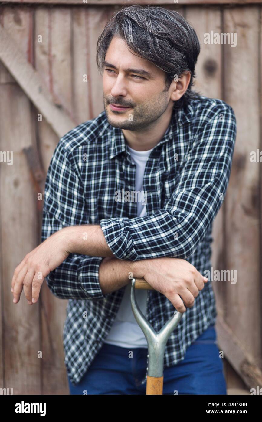 Un fermier pensif pendu sur une bêche contre une porte en bois Banque D'Images