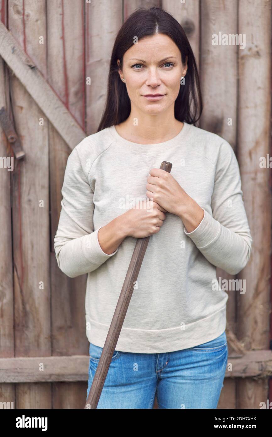 Portrait d'une fermière confiante debout contre une porte en bois Banque D'Images