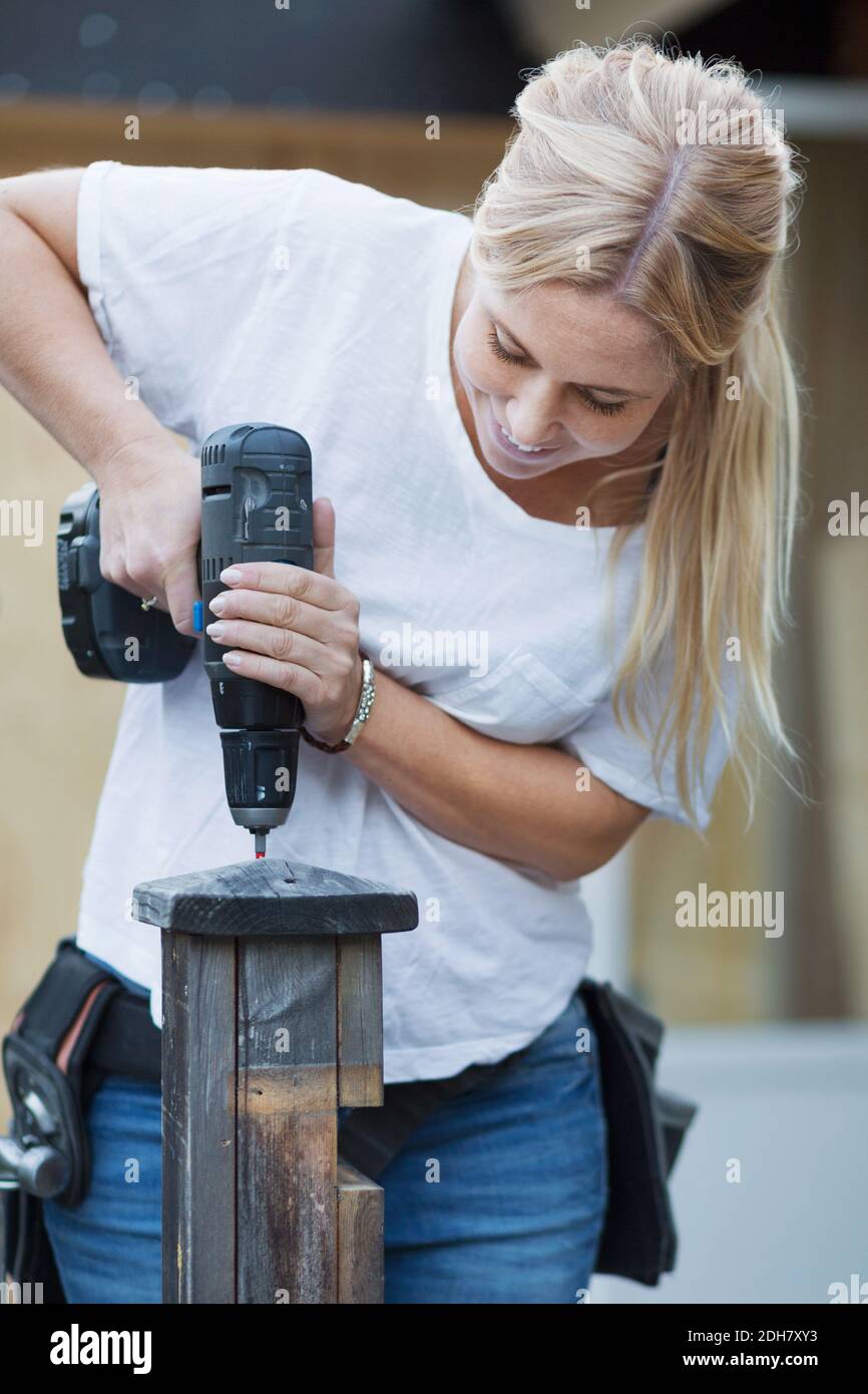 Bonne femme utilisant un tournevis sans fil sur un poteau en bois Banque D'Images