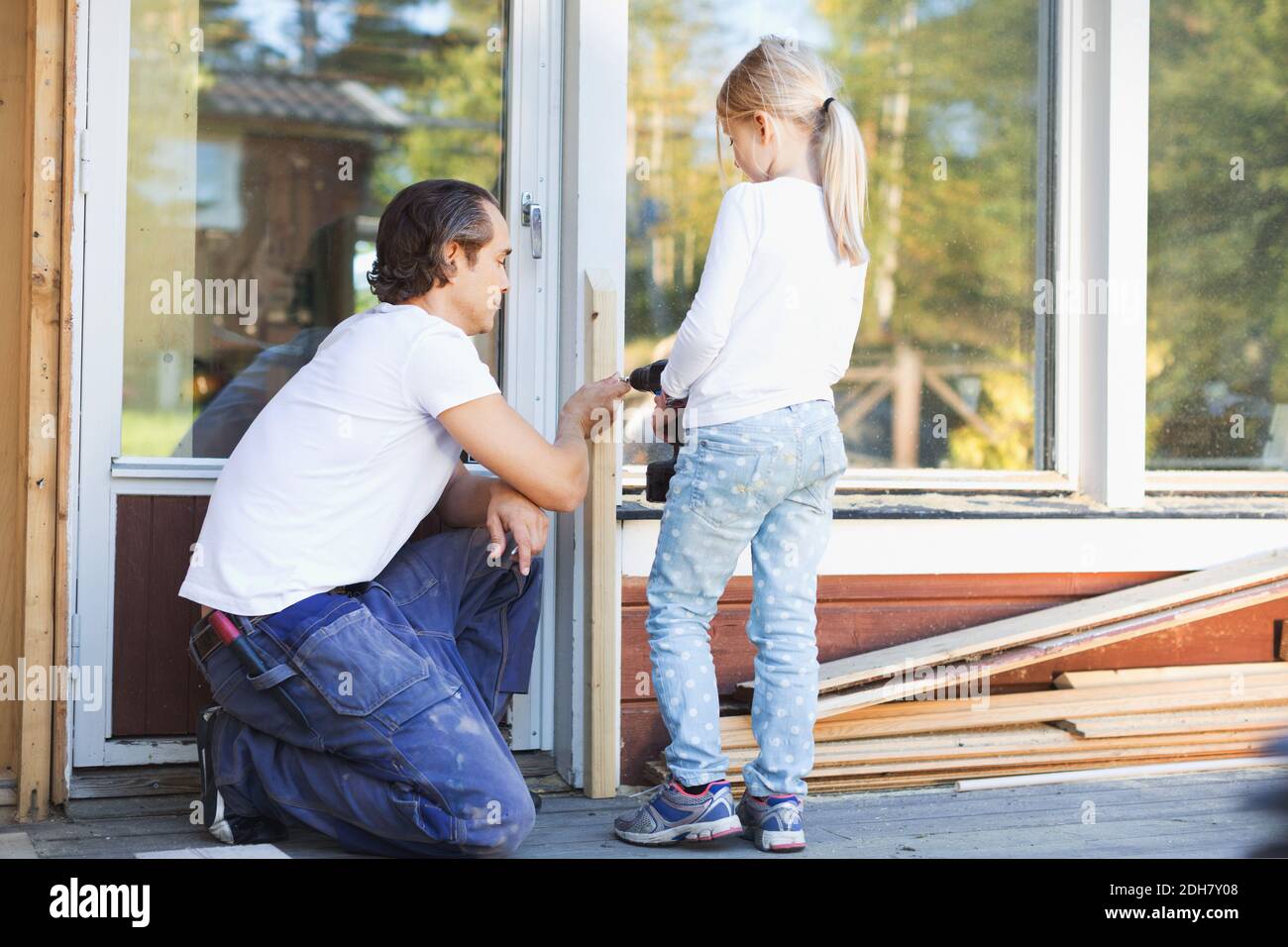 Père aidant la jeune fille à utiliser un tournevis sans fil sur le cadre pendant rénovation Banque D'Images