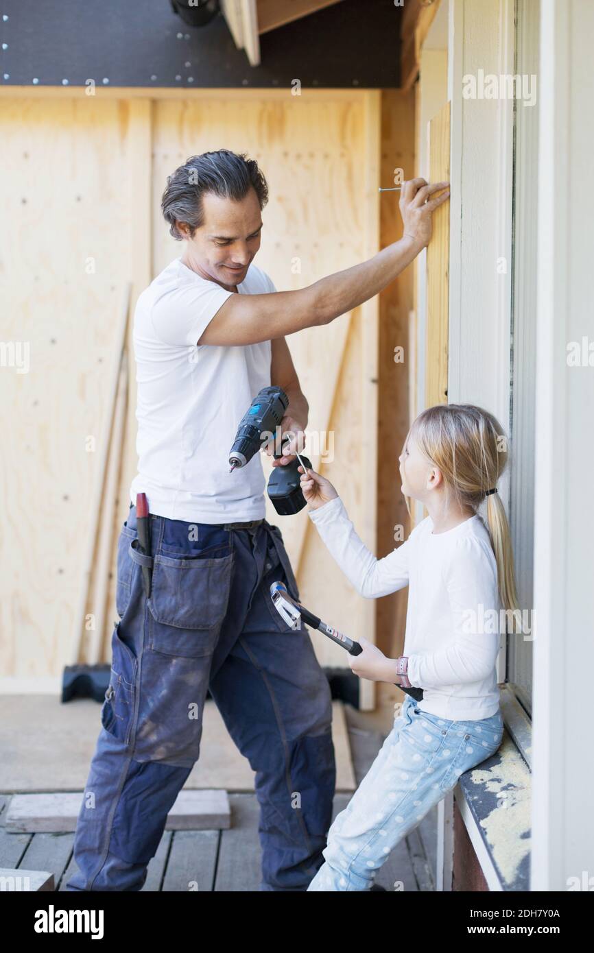 Fille passant l'ongle au père travaillant sur le cadre de fenêtre de maison en cours de rénovation Banque D'Images