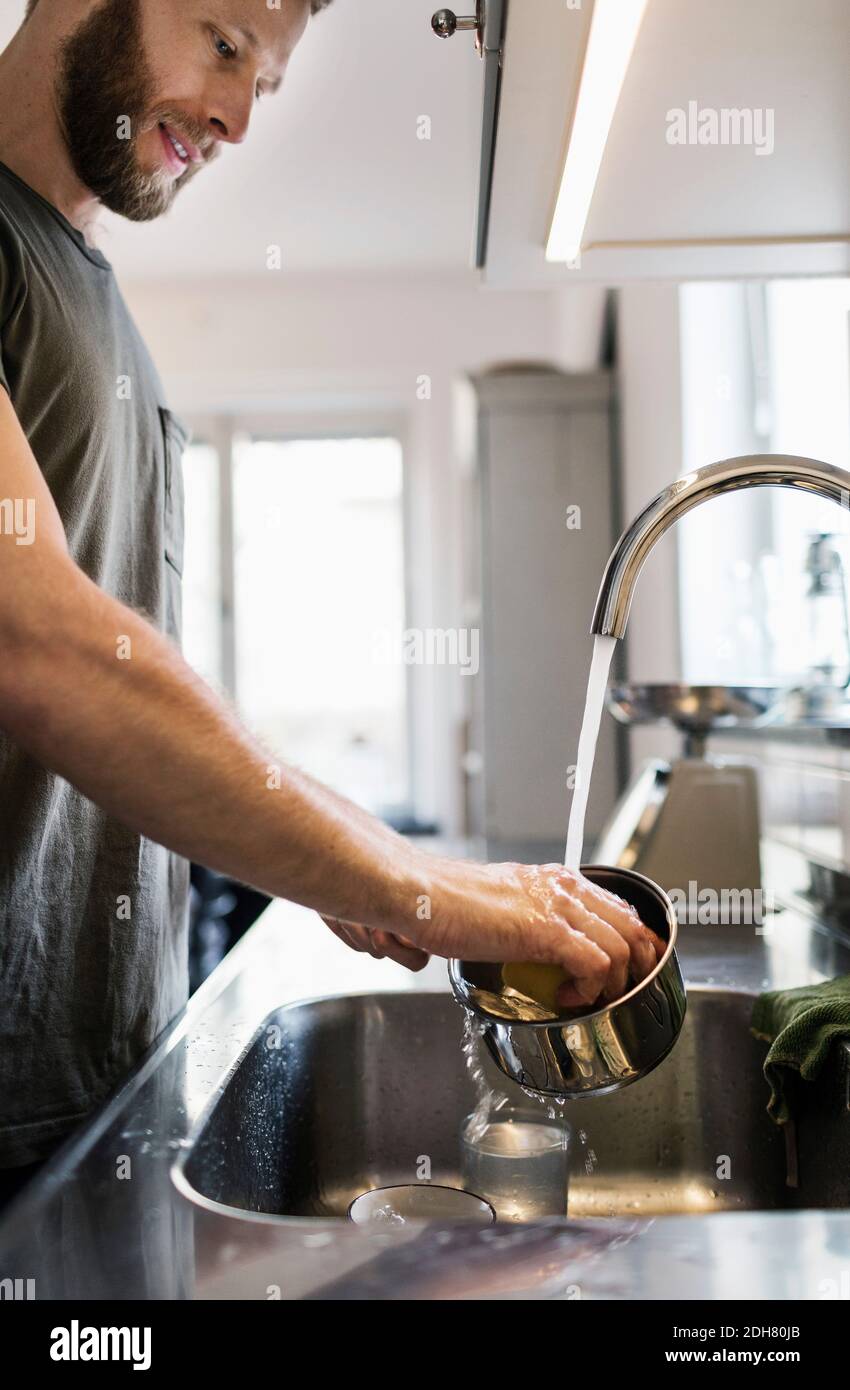 Homme lavant une casserole avec un tampon à récurer à l'évier Banque D'Images