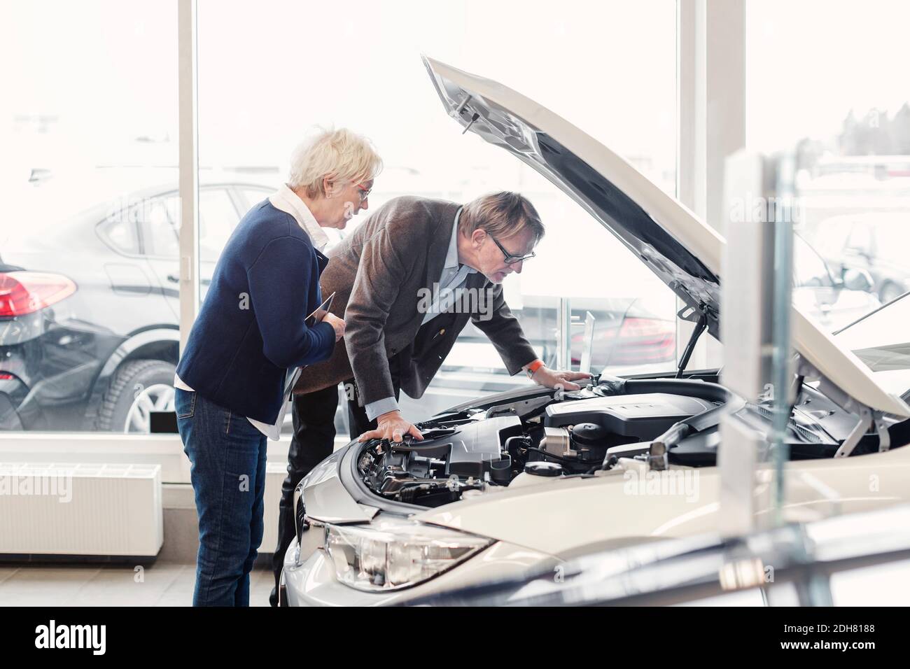 Un couple senior examine le moteur de la voiture dans la salle d'exposition Banque D'Images