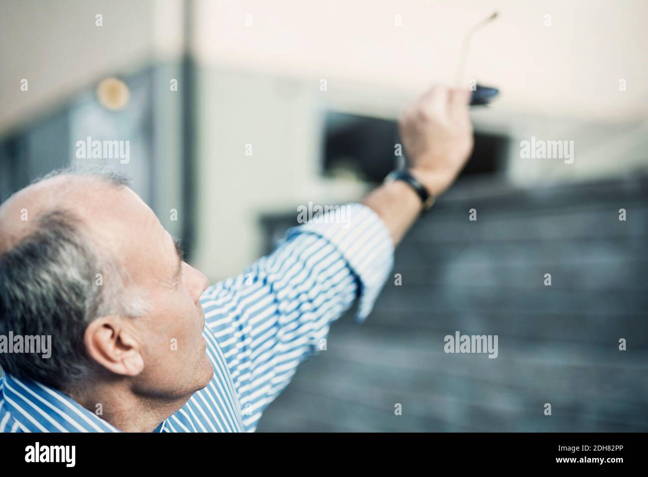 Homme mature tenant des lunettes de soleil tout en levant le bras à l'extérieur Banque D'Images