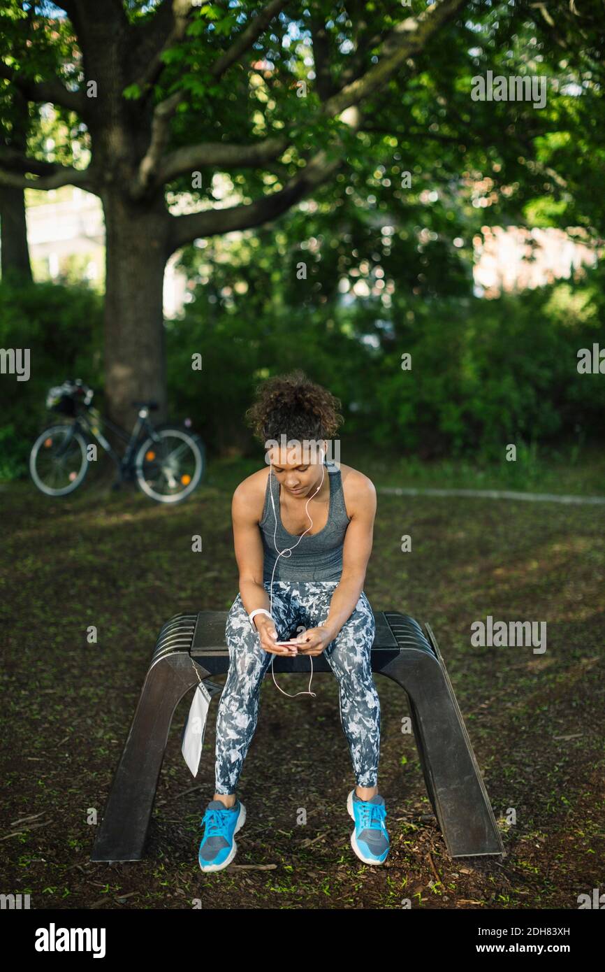 Femme assise au banc pour écouter de la musique dans le parc Banque D'Images