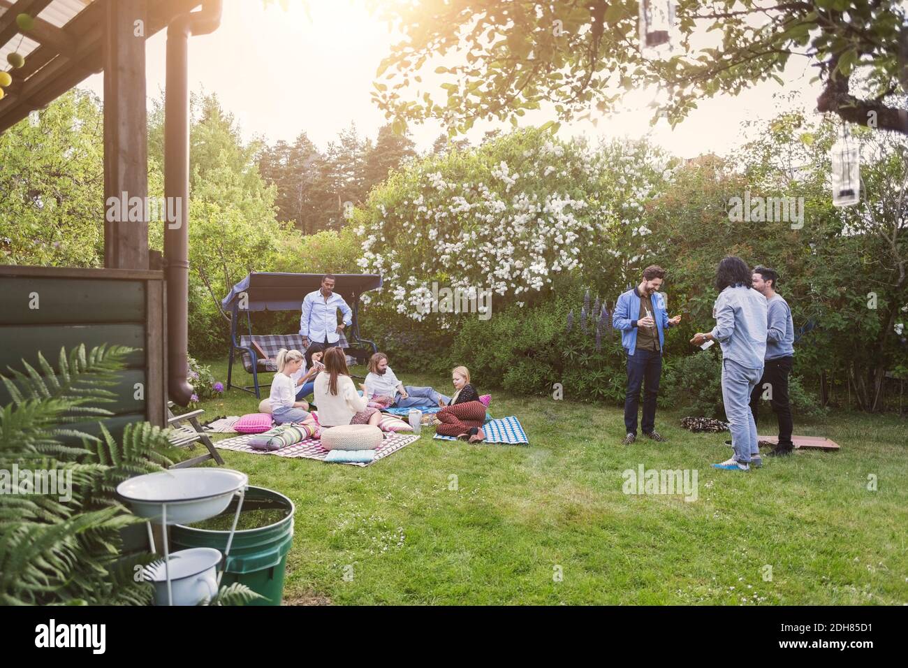 Des amis multi-ethniques commérages tout en ayant de la nourriture dans la pelouse pendant l'été fête Banque D'Images