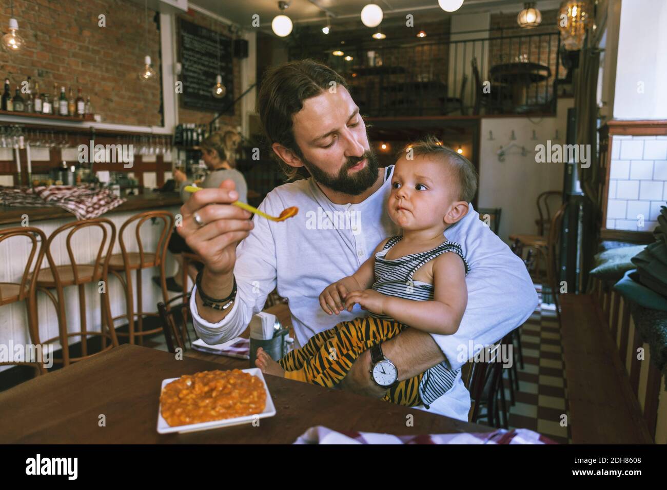 Homme adulte moyen nourrissant bébé garçon à la table du restaurant Banque D'Images