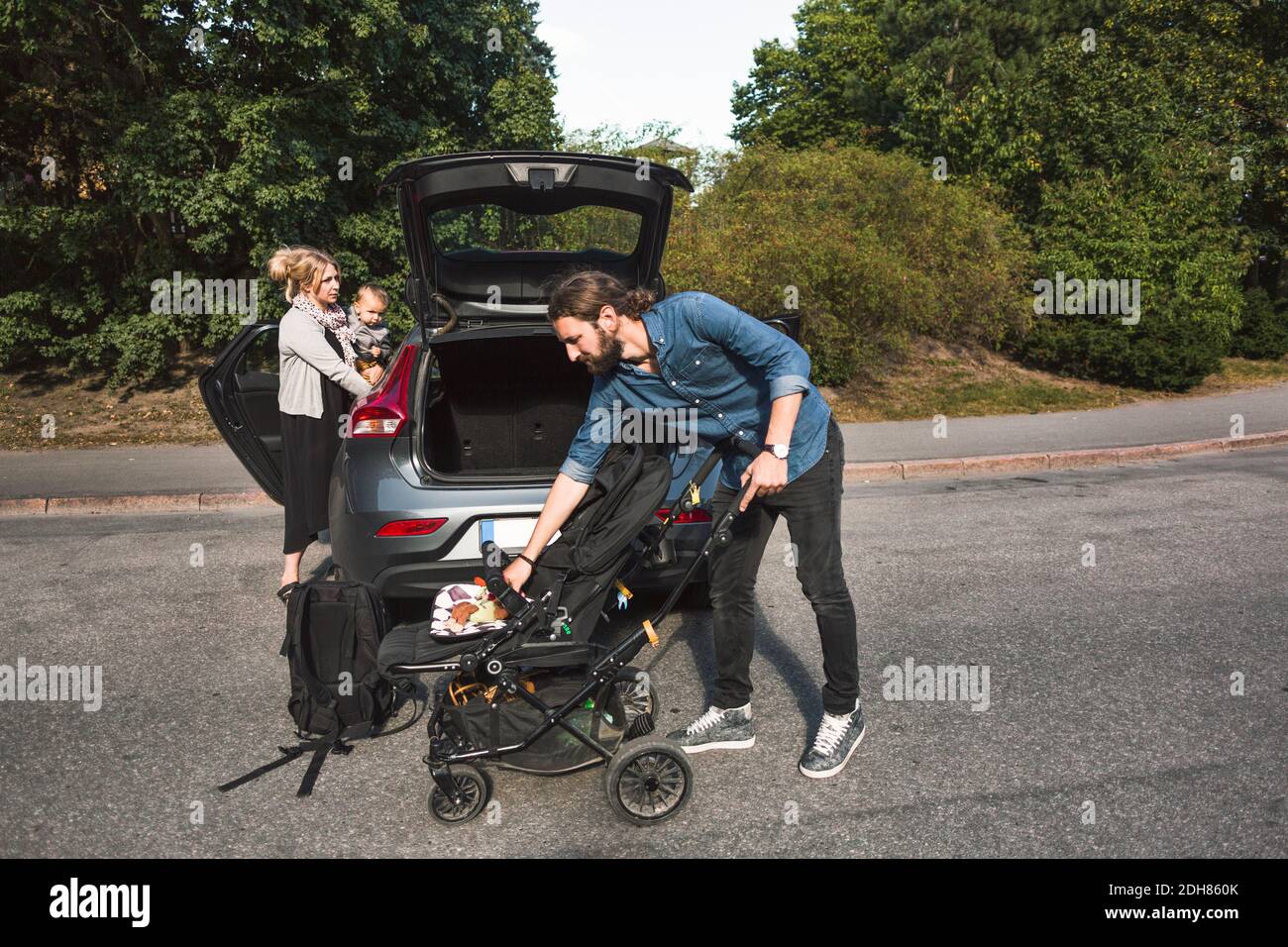 Parents d'adultes de taille moyenne avec bébé garçon et poussette près de la voiture sur la rue Banque D'Images