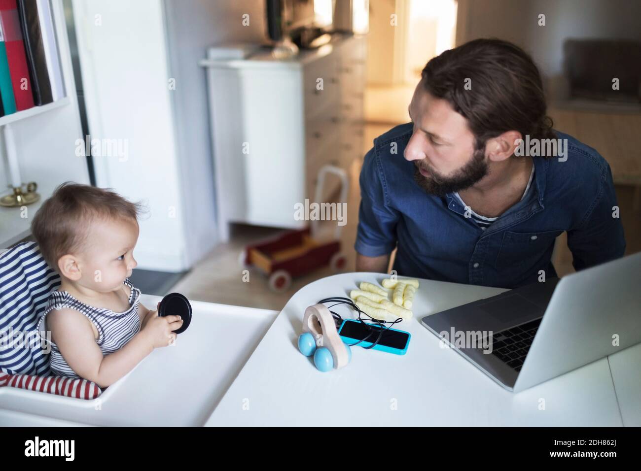 Homme adulte moyen prenant soin de bébé garçon avec un ordinateur portable sur table à la maison Banque D'Images