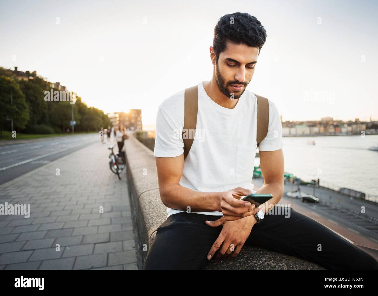 Un touriste utilise un smartphone tout en étant assis sur un mur de soutènement de pont Banque D'Images