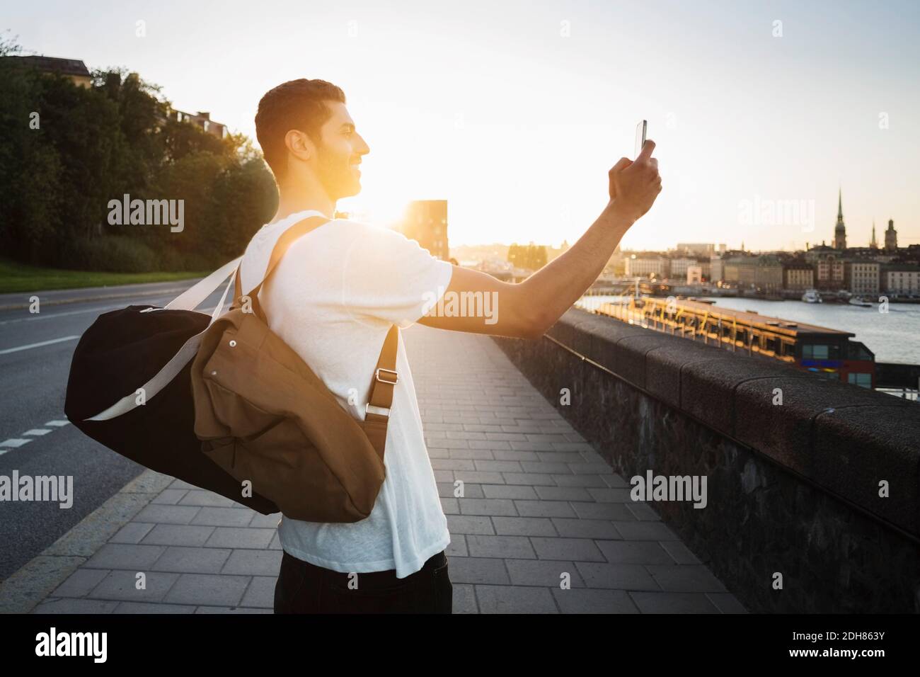 Vue latérale d'un touriste en train de photographier un smartphone debout sur le pont Banque D'Images