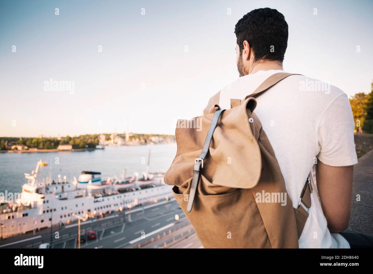 Vue arrière de touriste mâle avec sac à dos assis sur la retenue mur du pont Banque D'Images