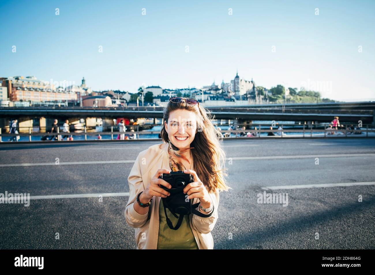 Portrait d'un touriste heureux tenant l'appareil photo sur le pont contre clair ciel Banque D'Images