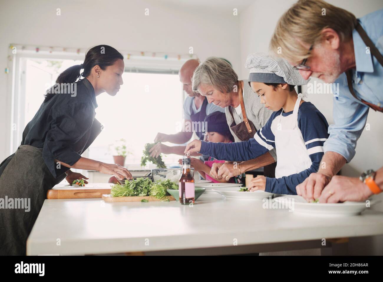 Femme guidant la famille dans la préparation de la cuisine asiatique Banque D'Images