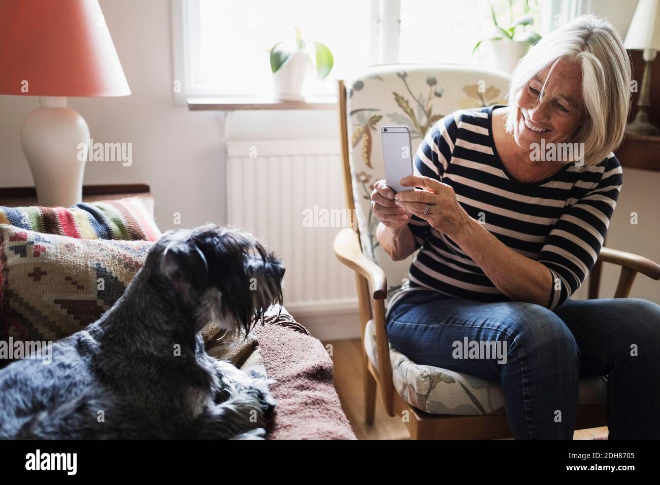 Bonne femme âgée qui photographie son chien avec un smartphone à la maison Banque D'Images