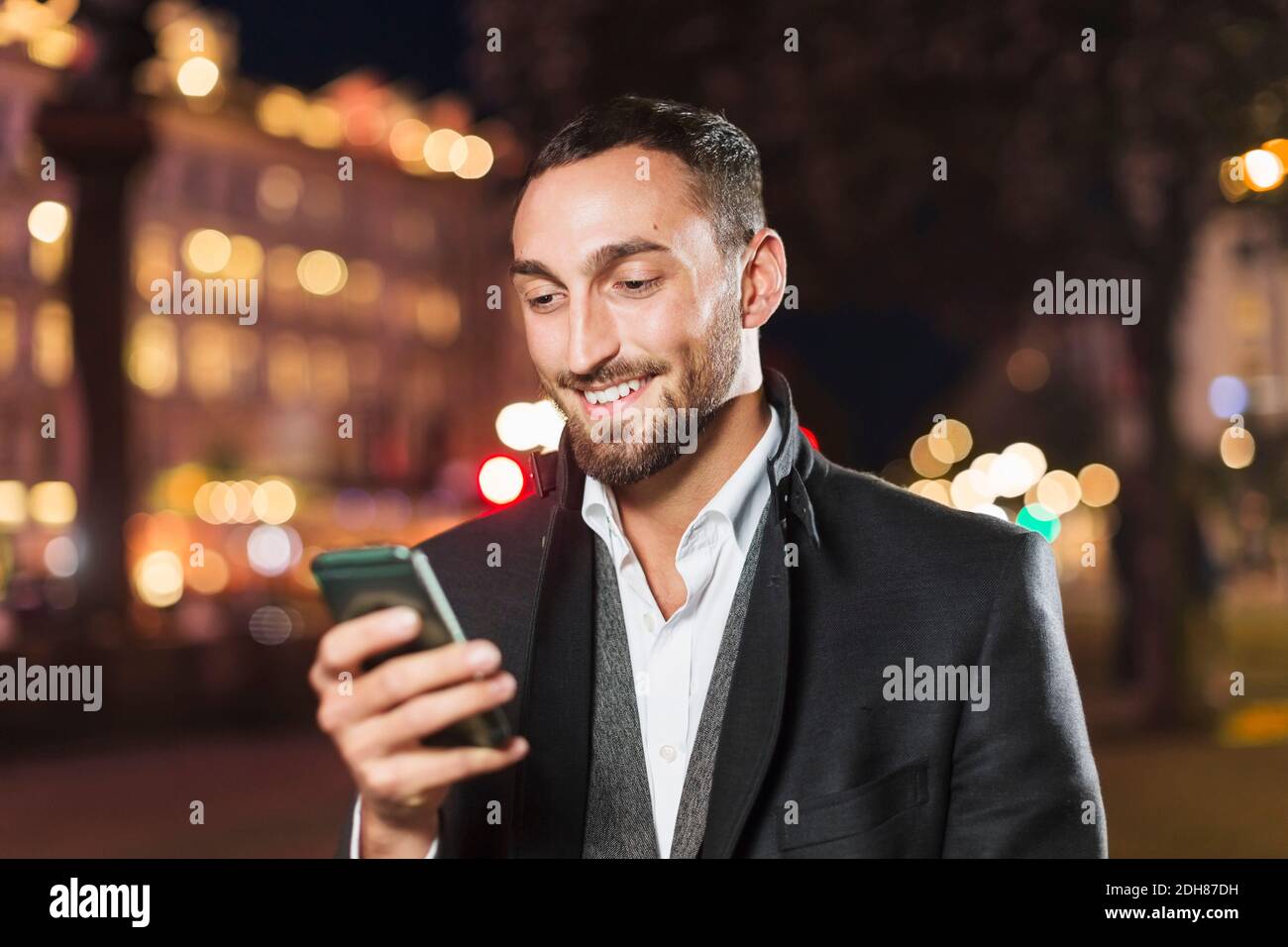 Un homme heureux utilisant un smartphone dans la ville la nuit Banque D'Images