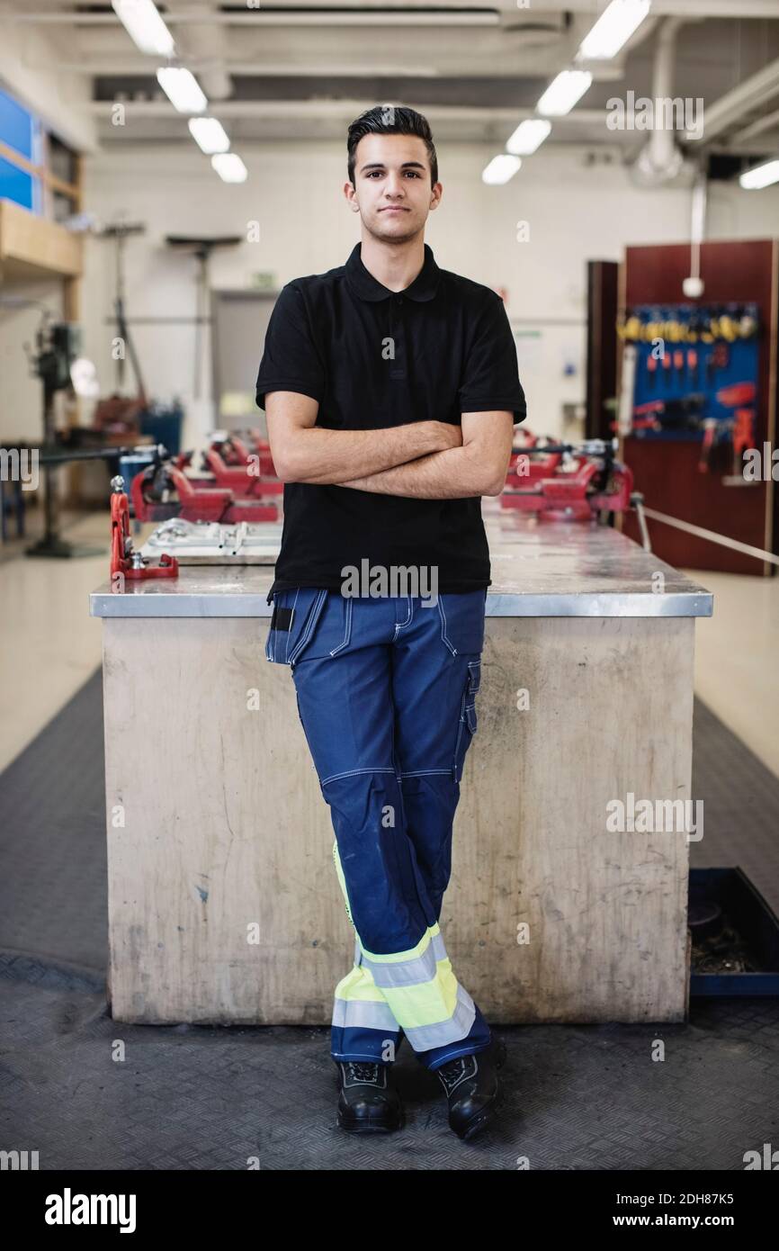 Portrait complet d'un étudiant en mécanique automobile homme confiant debout bras croisés dans l'atelier Banque D'Images