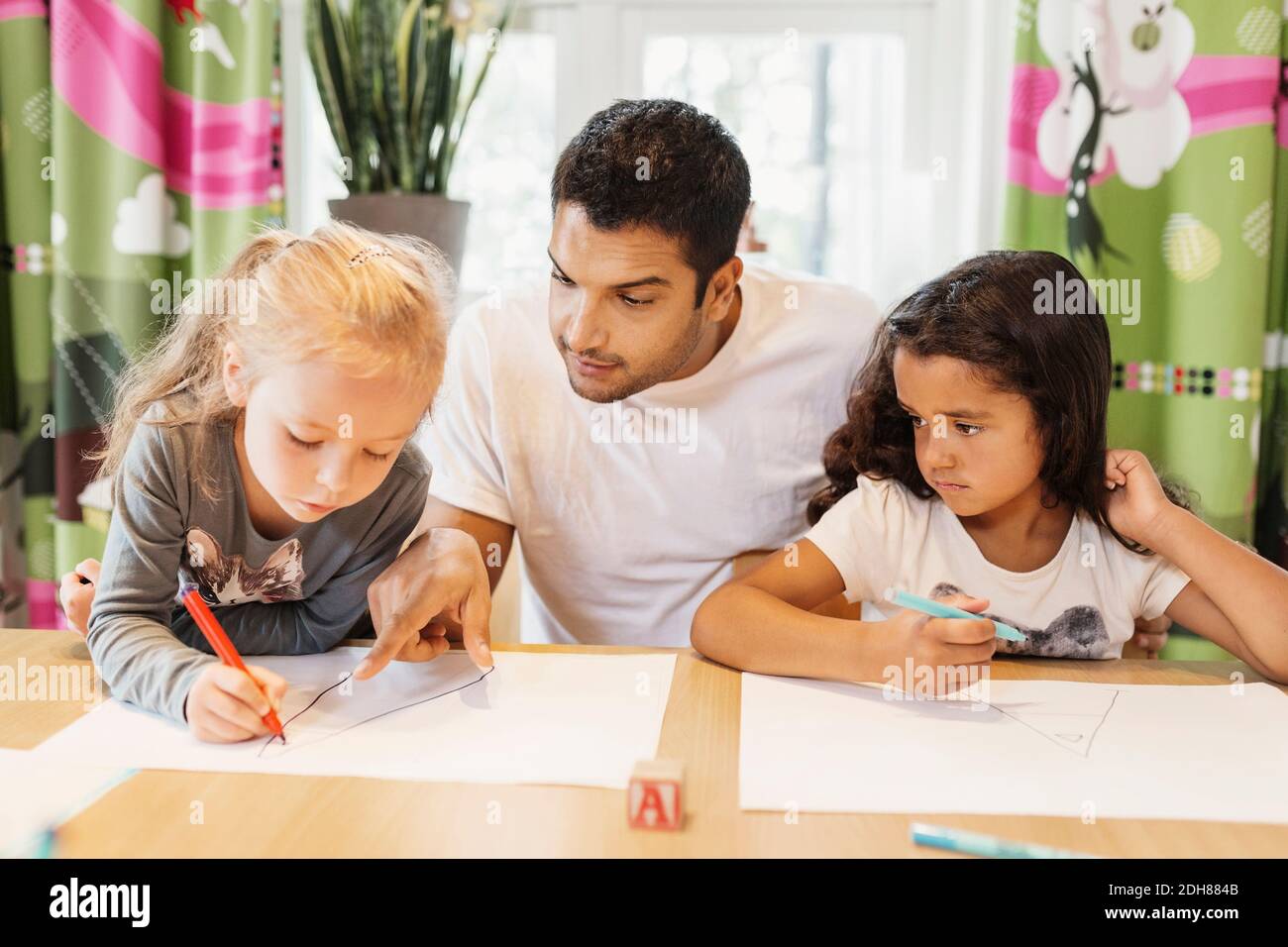 Professeur d'adulte de taille moyenne aidant les étudiantes à dessiner à l'école maternelle Banque D'Images