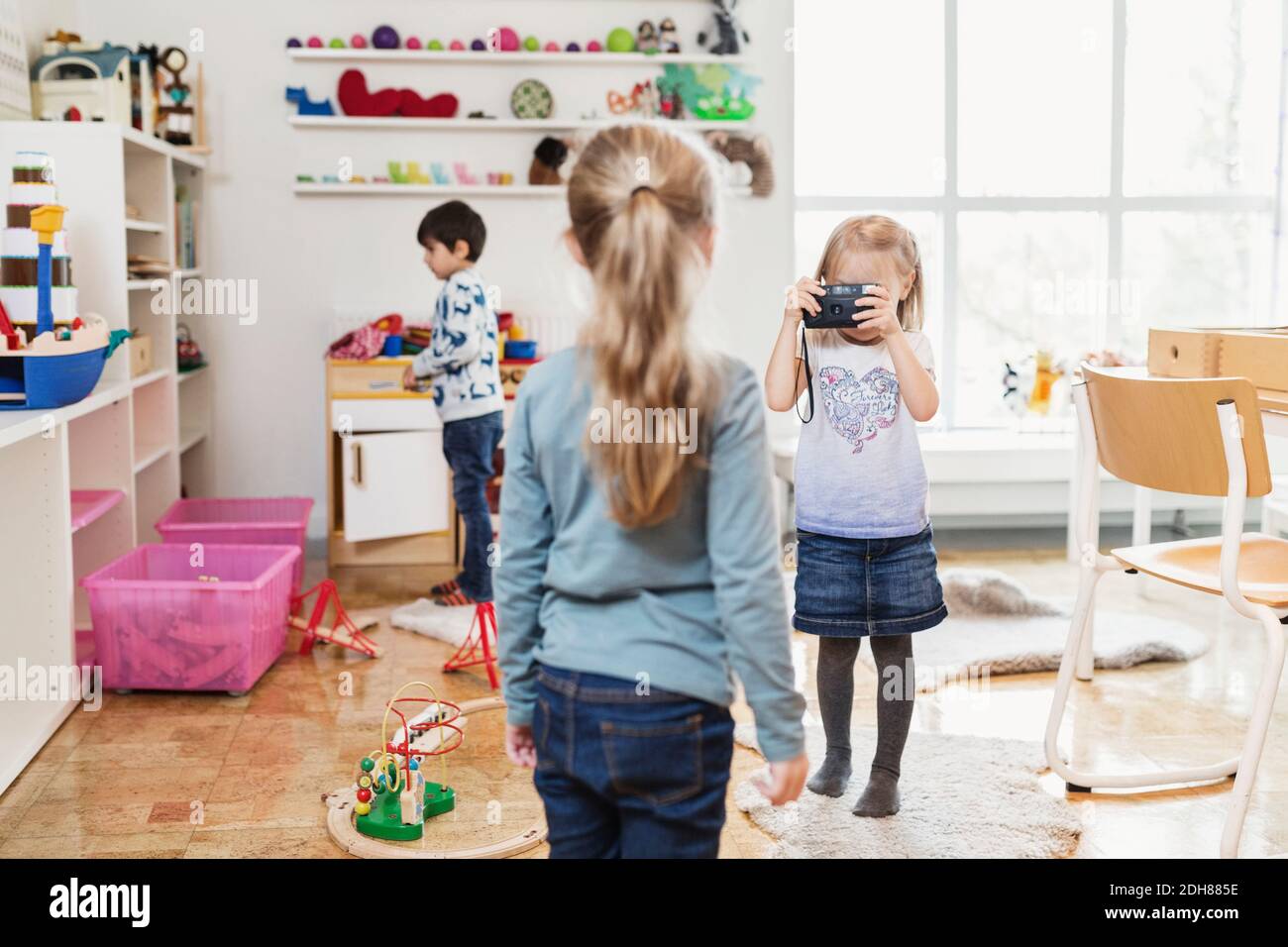 Petite fille prenant la photo d'un ami à travers un appareil photo jouet dans la salle de classe Banque D'Images
