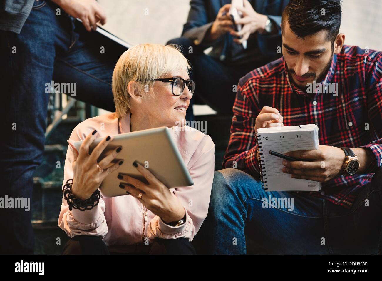 Professionnels avec bloc-notes et tablette numérique assis sur des marches au bureau Banque D'Images