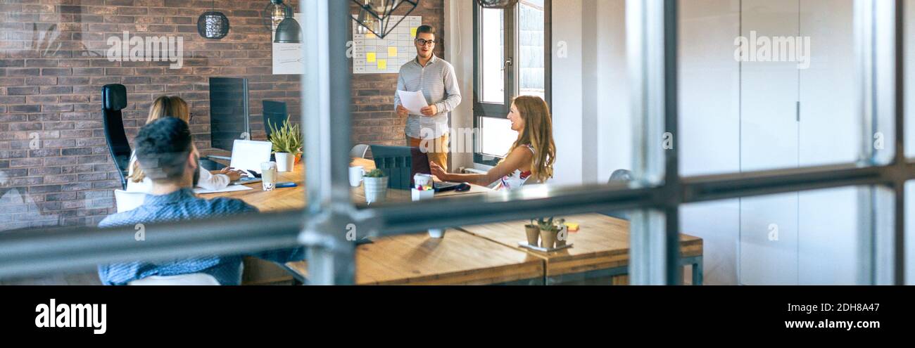 Jeune entraîneur donnant une discussion aux travailleurs dans un moderne bureau Banque D'Images