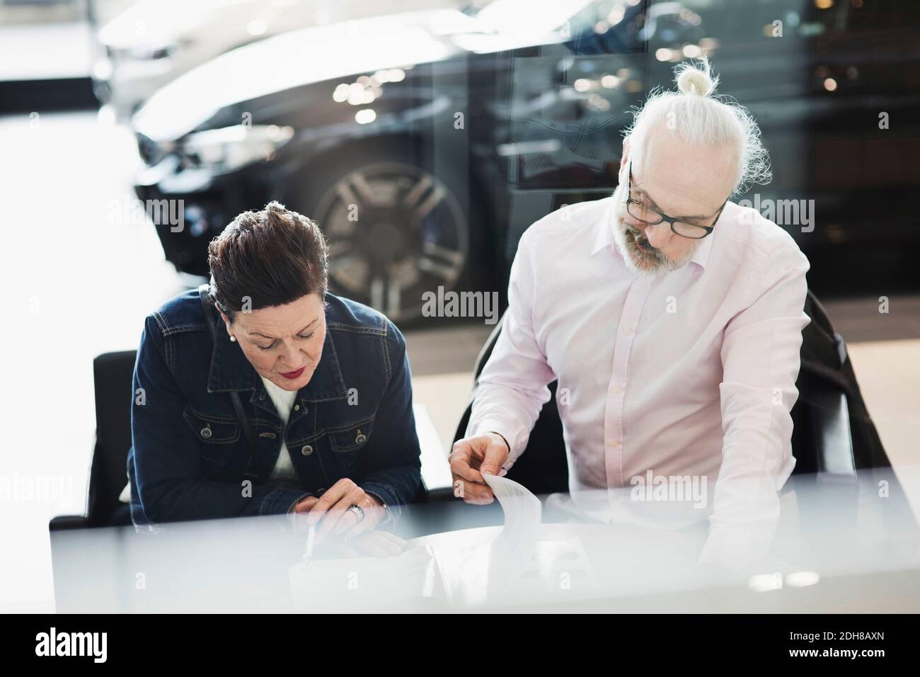 Homme et femme senior lisant des documents en étant assis en voiture salle d'exposition Banque D'Images