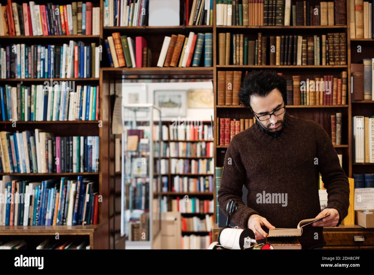 Livre de lecture du bibliothécaire en se tenant contre les étagères Banque D'Images