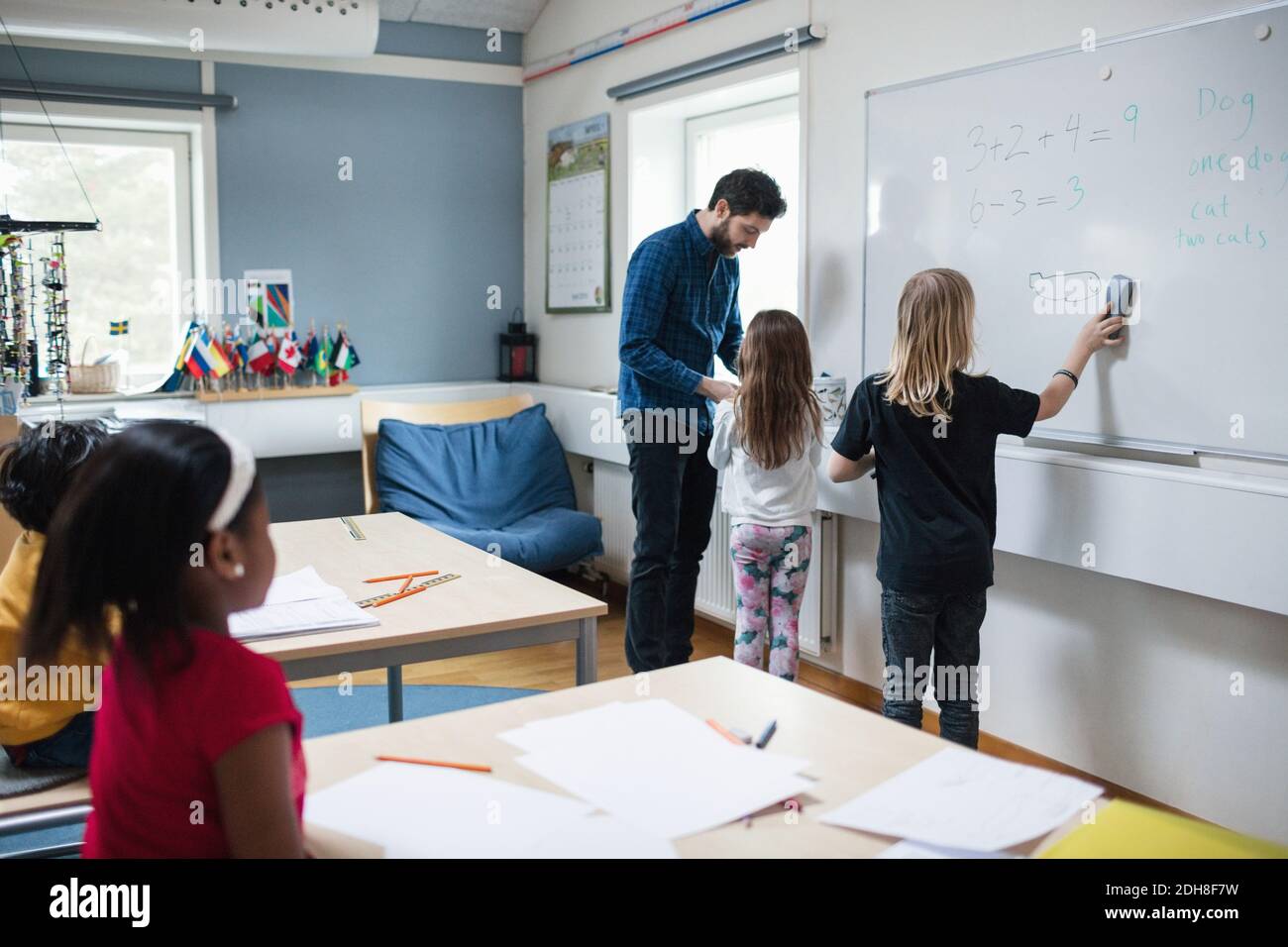 Fille parlant à l'enseignant pendant que l'élève dessine sur le tableau blanc dans salle de classe Banque D'Images