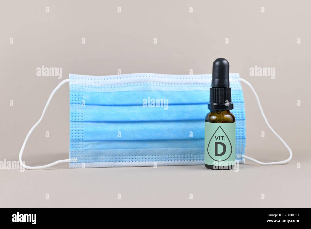 Concept pour la vitamine D aider à combattre la maladie du virus Corona avec masque médical et bouteille avec gouttes de vitamine sur le gris arrière-plan Banque D'Images